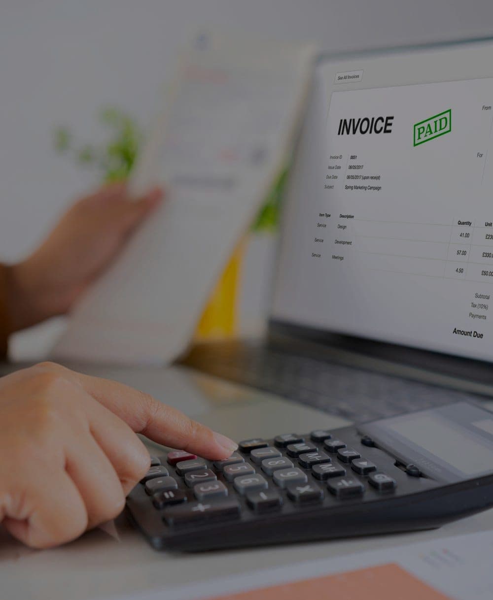 A paid invoice checked off beside a desk calculator and laptop